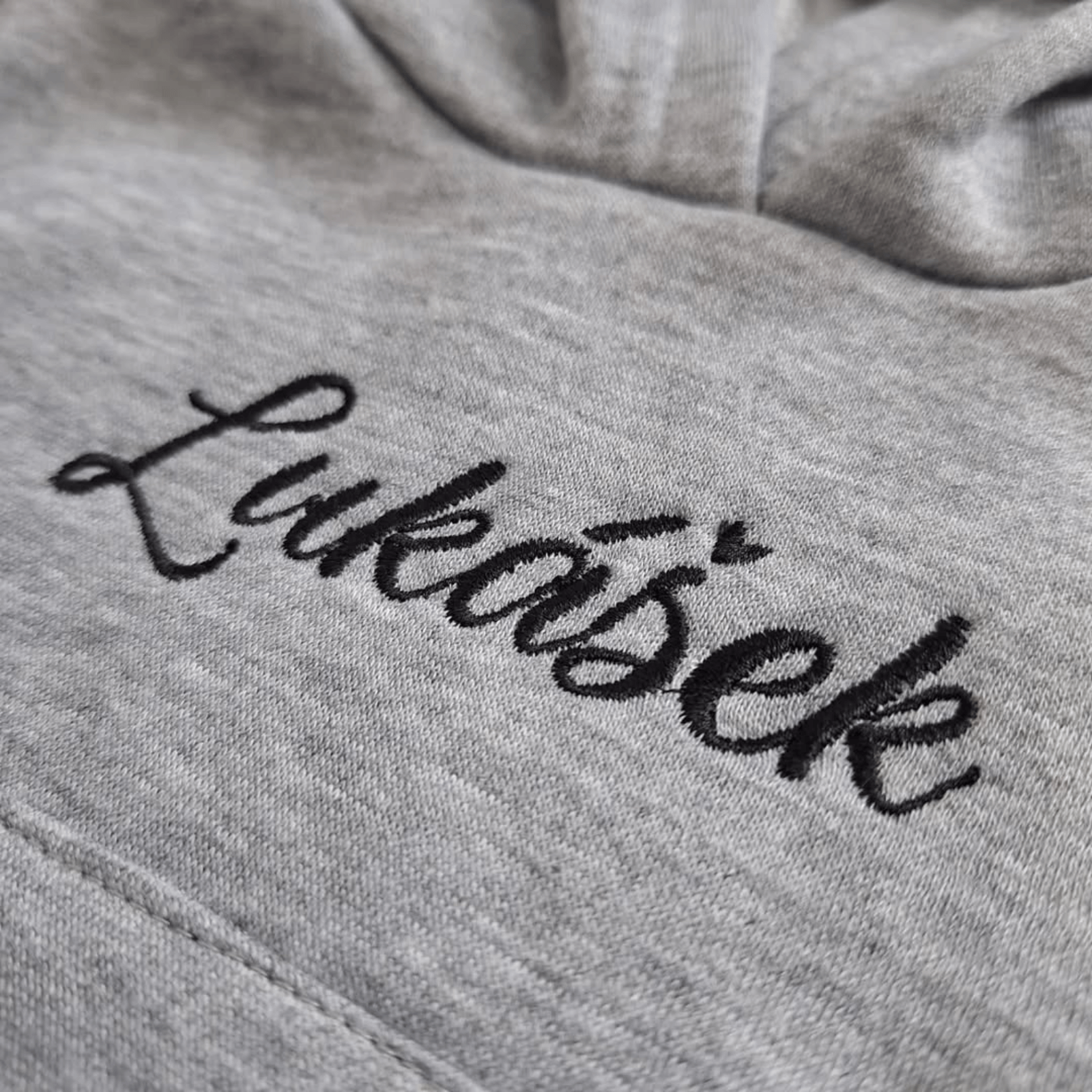 Měkká šedá kojenecká mikina s kapucí a personalizovanou černou výšivkou jména Lukášek.