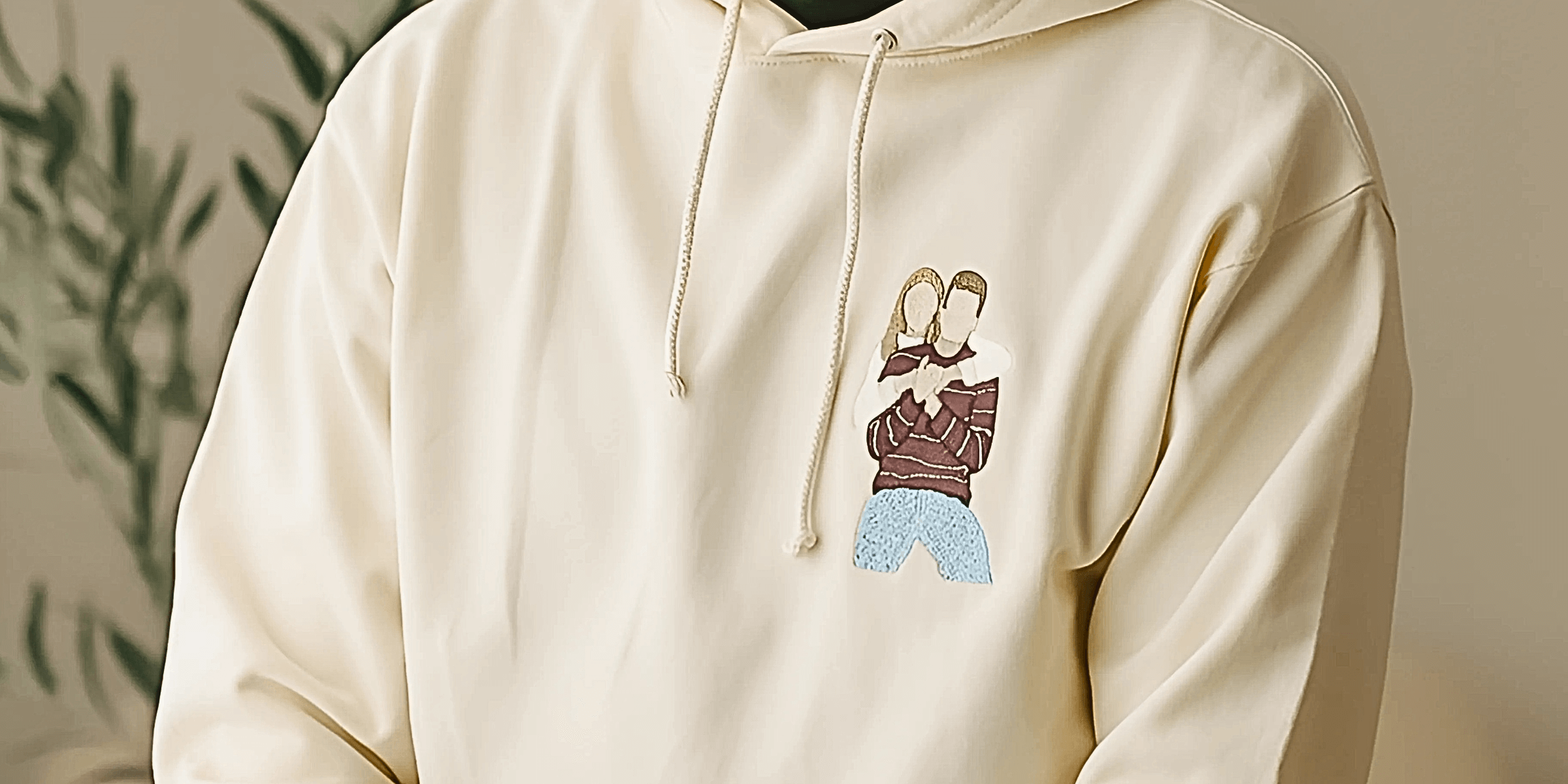 Detailní záběr na krémovou mikinu s výšivkou barevné siluety objímajícího se páru na hrudi