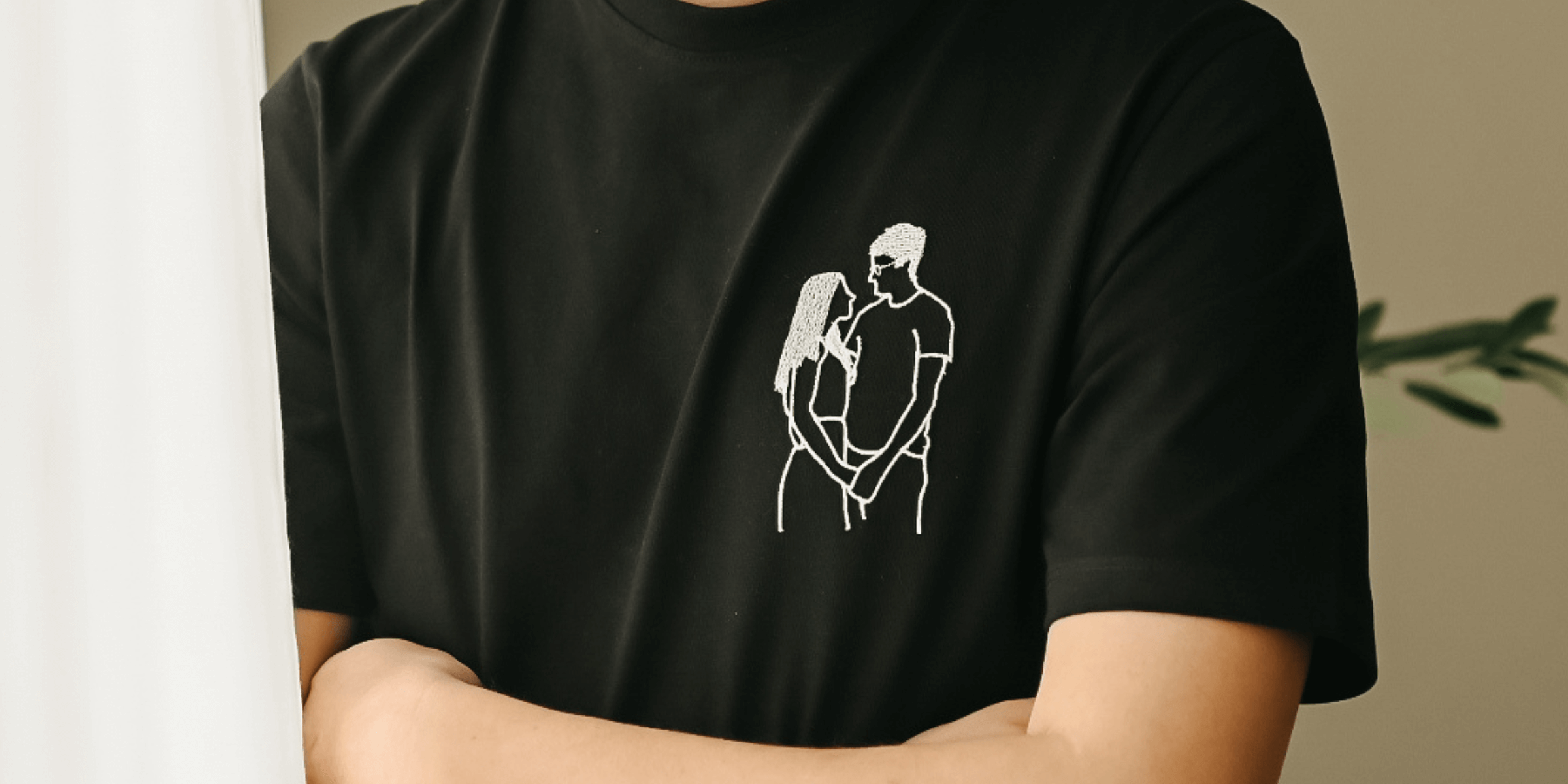 Detailní záběr na černé triko s výšivkou jednobarevného obrysu objímajícího se páru na hrudi